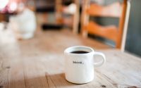 Picture of white coffee cup with the words "Begin" on a table.