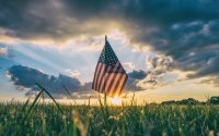 Picture of an American Flag amidst a blue sky and green grass